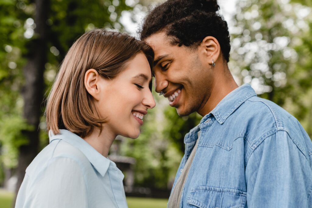 Young mixed-race couple going to kiss each other embracing hugging walking in city park