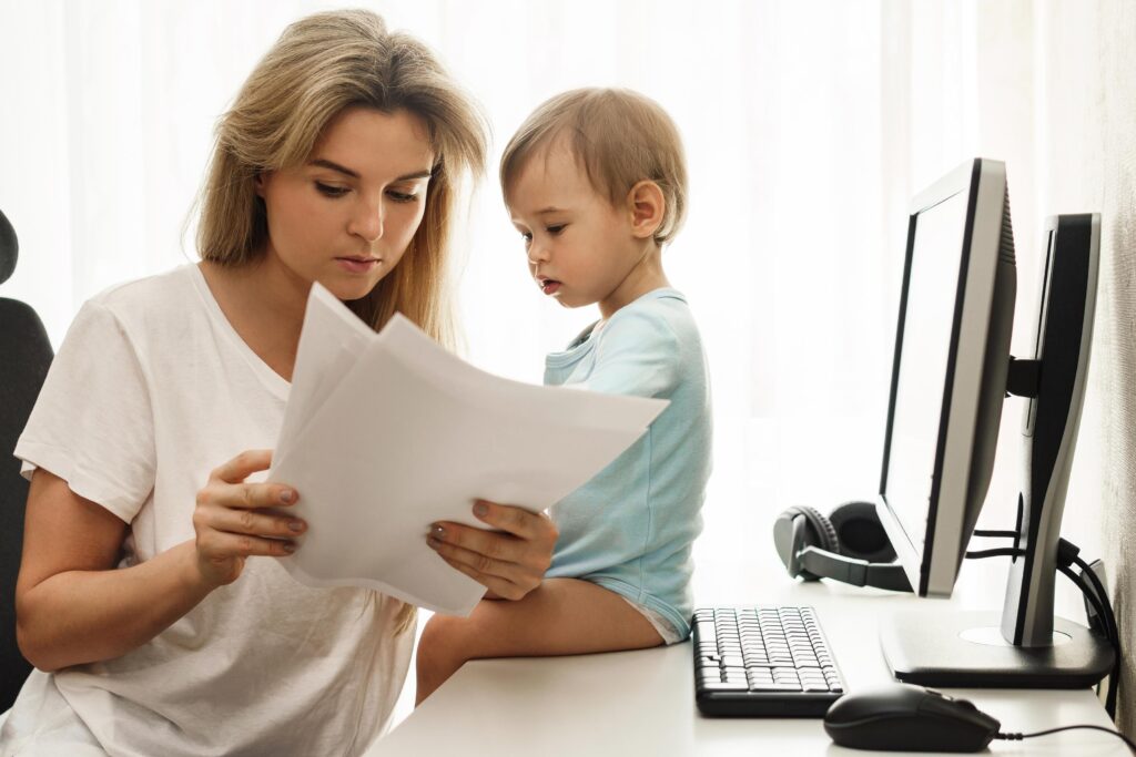 Young freelancer mother reading papers at home office with son s