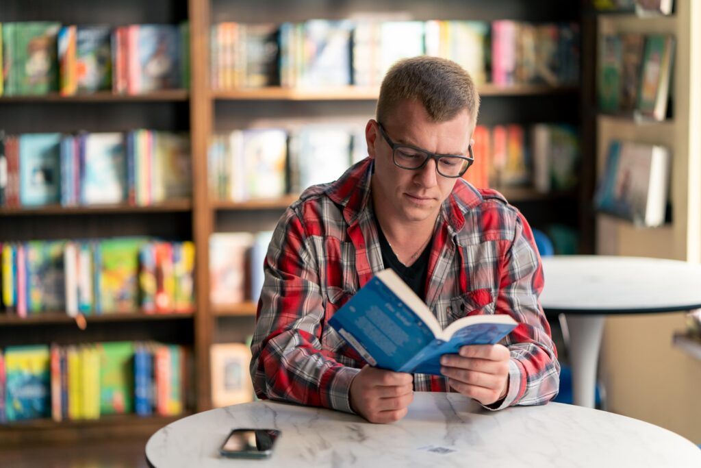 male professor in glasses sits in a scientific and technical library reads a book and prepares write a dissertation