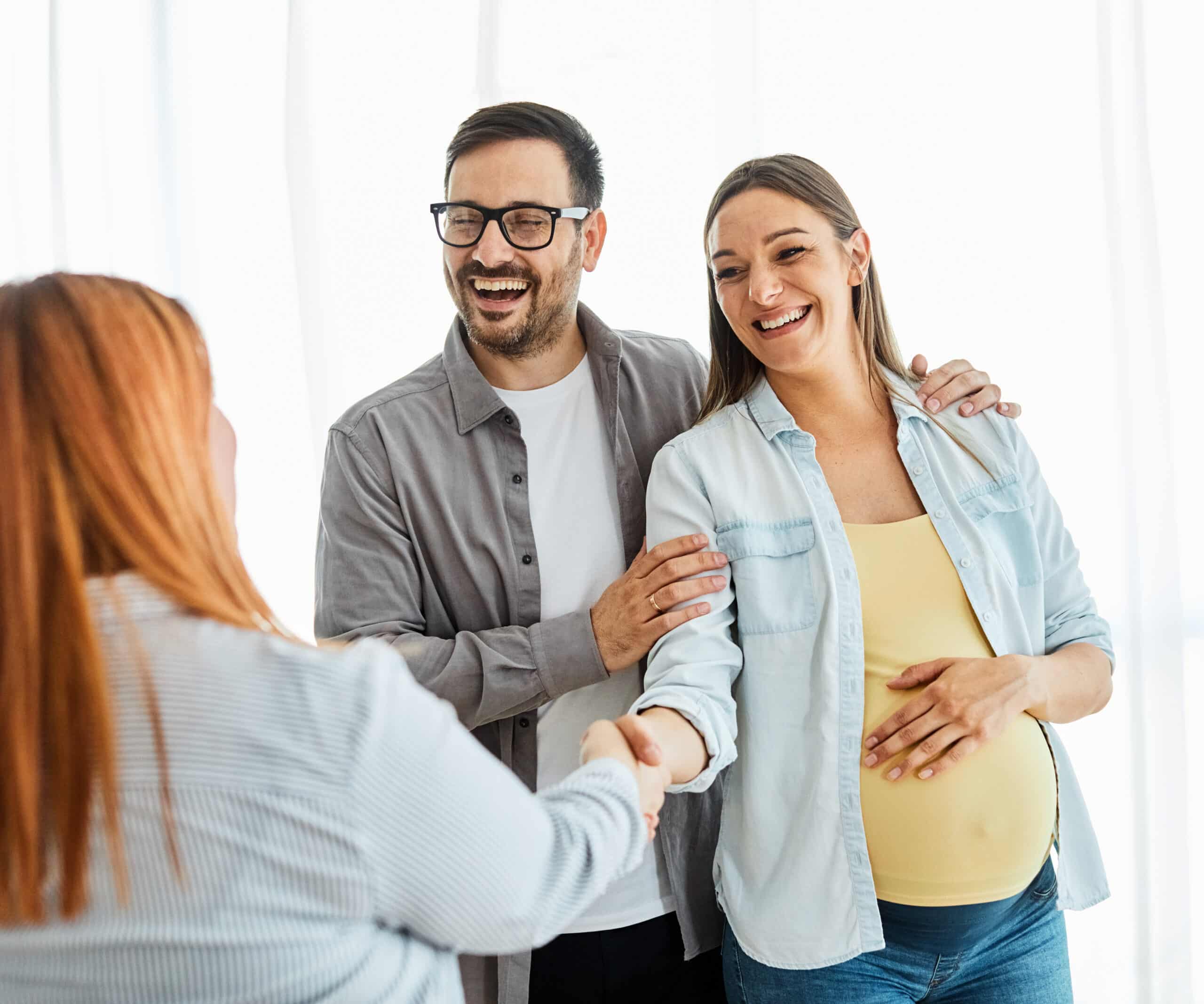 Young happy couple, a pregnant woman, and an agent shaking hands in a new property