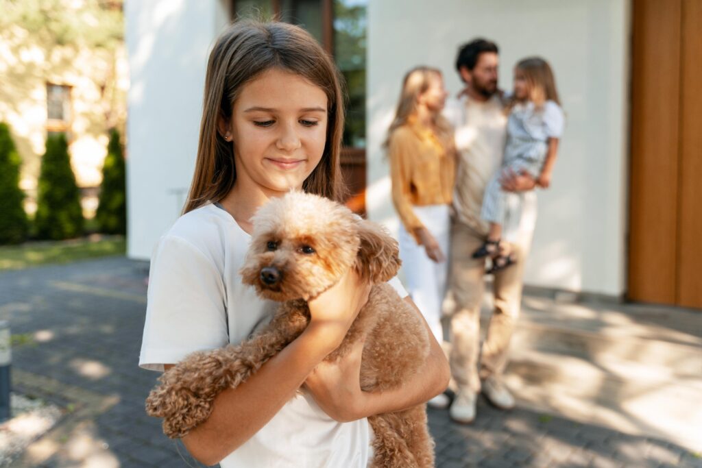 Happy cute girl holding toy poodle with family in background outside home