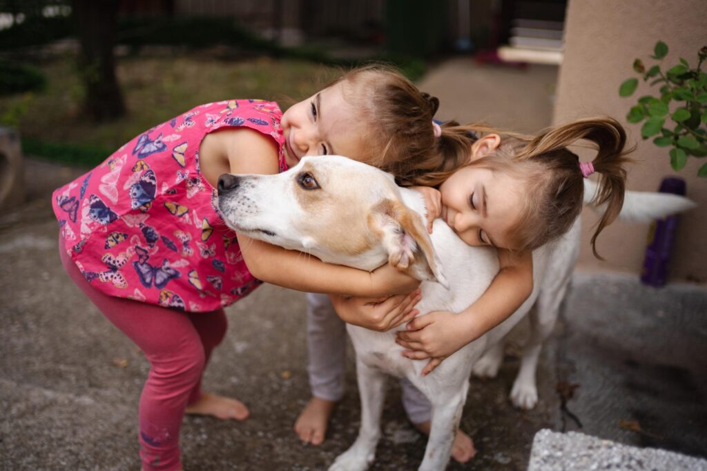 Joyful girls share a big hug with their playful dog outdoors