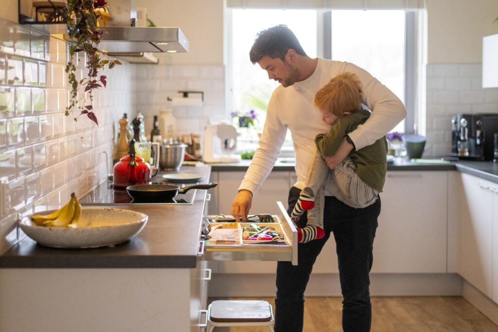 A tender moment in the kitchen as a man carries a young child while preparing a meal.