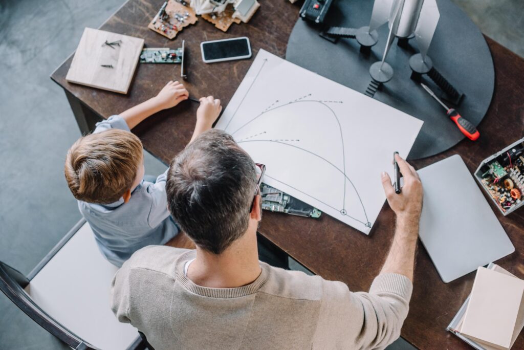 overhead view of father and son looking at blueprint for modeling rocket at home