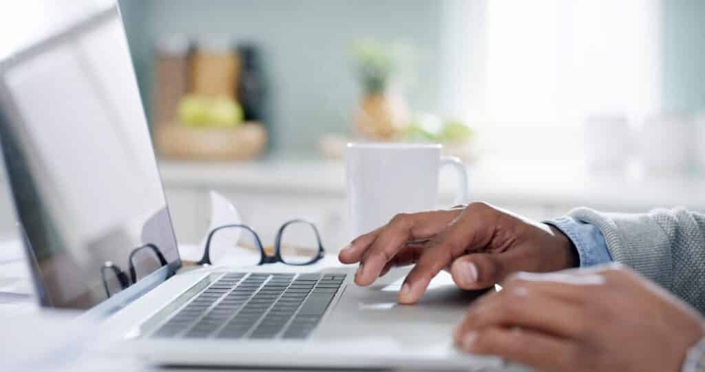 A person's hands are on a silver laptop in a home setting.