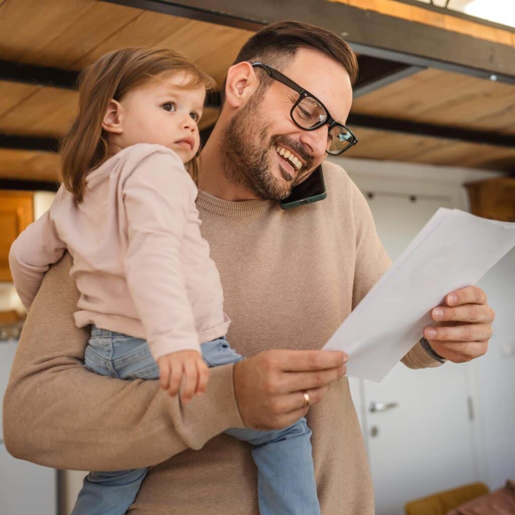 Smiling Father Working From Home While Holding His Toddler Child